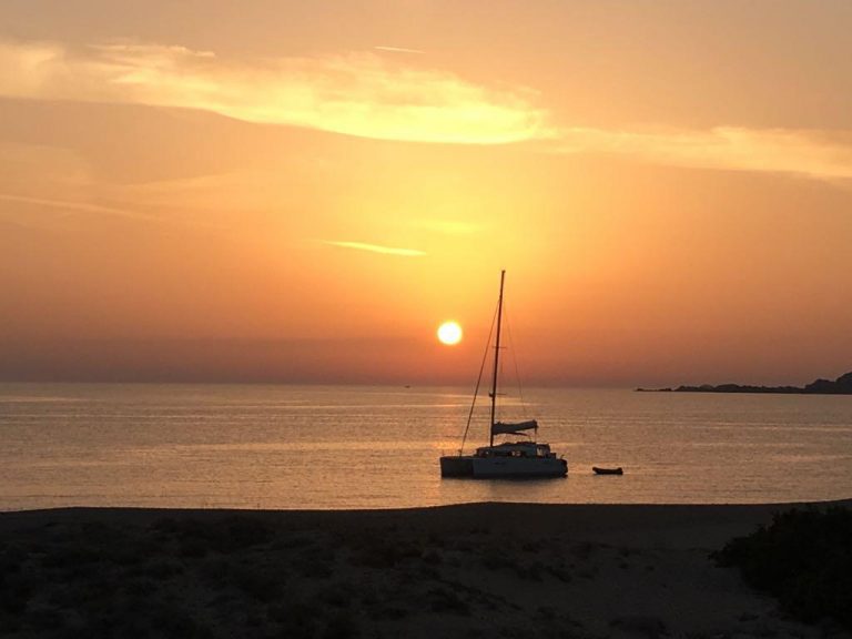 Żaglówka płynie po spokojnym morzu na tle zachodzącego słońca.